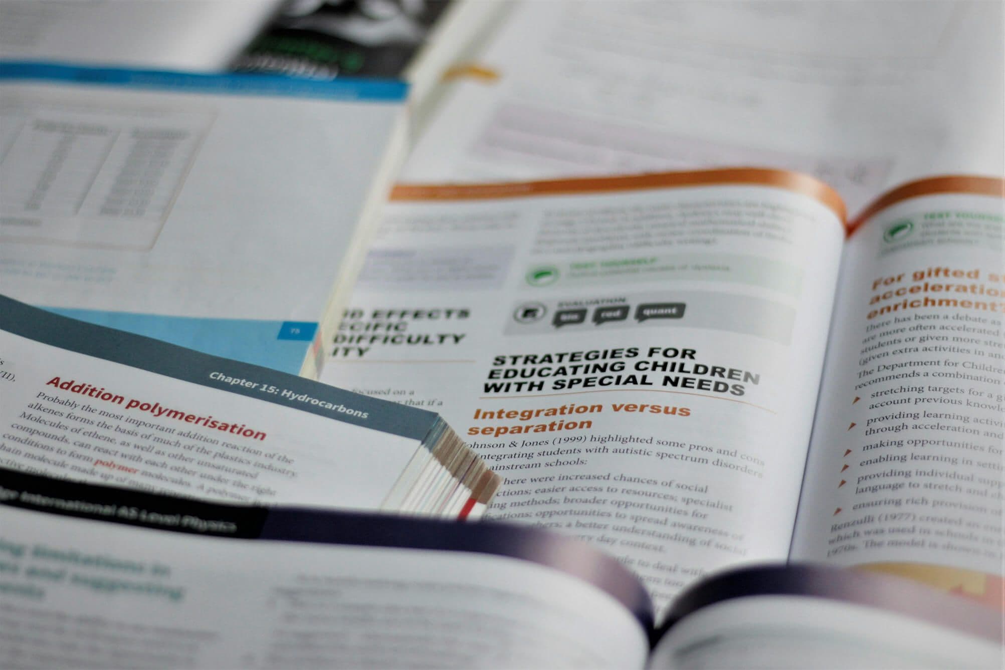 Otwarte podręczniki i publikacje naukowe ułożone jeden na drugim na biurku