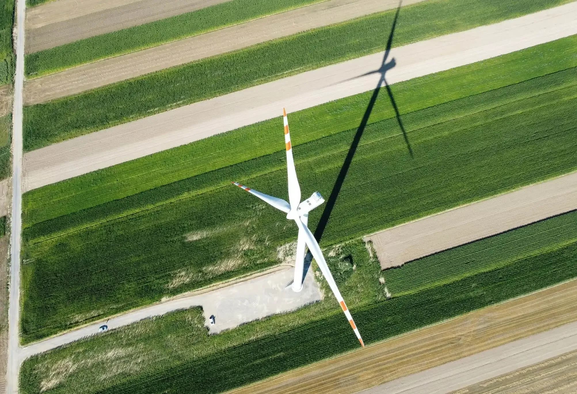 Turbina wiatrowa pośród pasów pól uprawnych, widok z drona z cieniem śmigieł