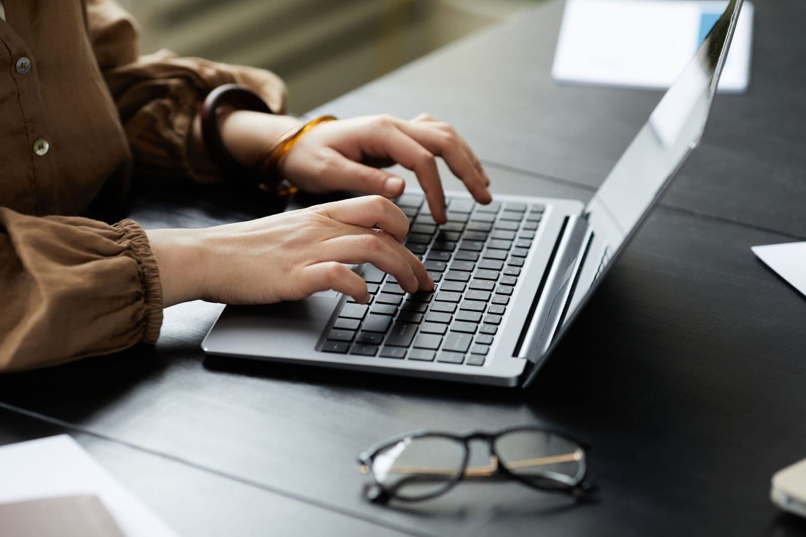 Osoba pisze na laptopie, obok leżą okulary
